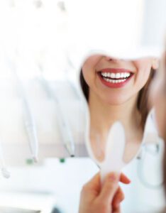 A female patient at Banyule Dental is holding a mirror and smiling