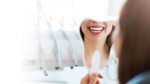 A female patient at Banyule Dental is holding a mirror and smiling
